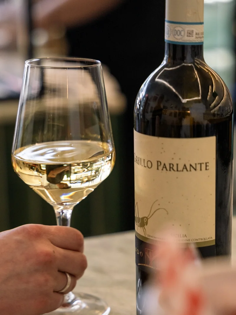A glass of Sicilian white wine beside the bottle on the table at Gemelli
